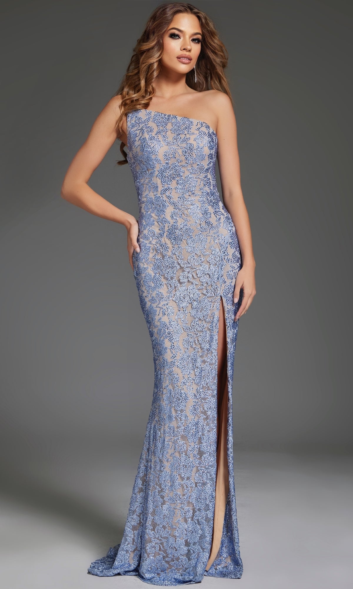 A woman models the Jovani 43753 long prom dress, a blue, one-shoulder gown with lace details and a high leg slit, standing against a plain gray background.